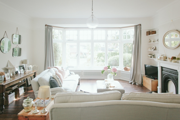 wohnzimmer im landhausstil weiße dekorationen, zwei weiße sofas, großes fenster, deko an der wand, spiegel