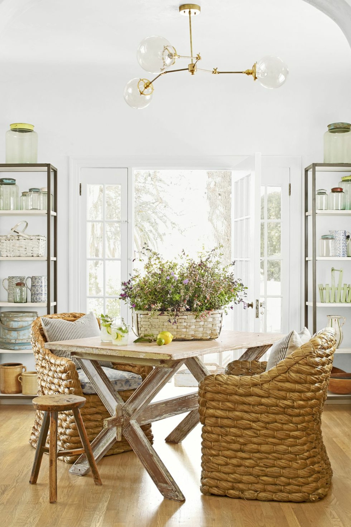 landhausmöbel designer ideen für ein gemütliches zuhause, zwei große stühle aus rattan und ein kleiner hocker, holztisch vintage, blumenkorb mit feldblumen