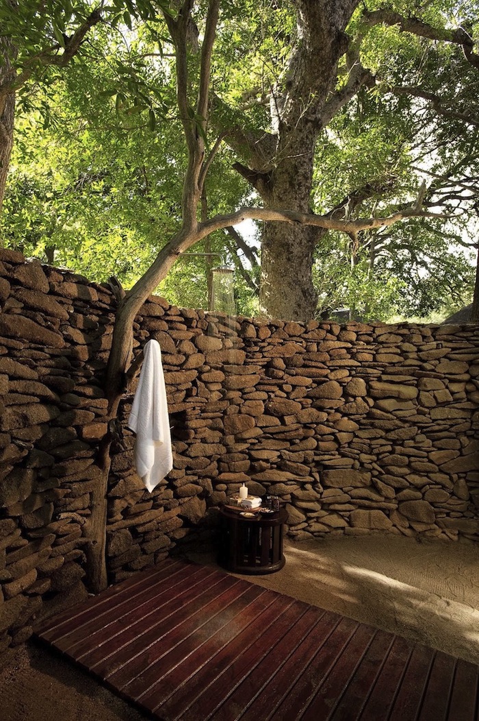 brauner boden aus holz im garten mit einer dusche, bäumen und wänden aus steinen, sichtschutz für gartendusche 