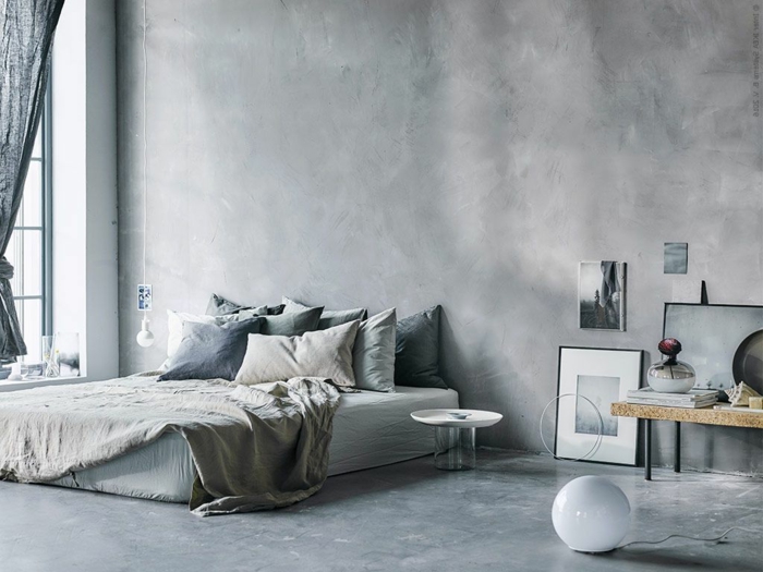 Schlafzimmer mit Betonboden, graue Wände, eine graue Matratze und graue Bettwäsche