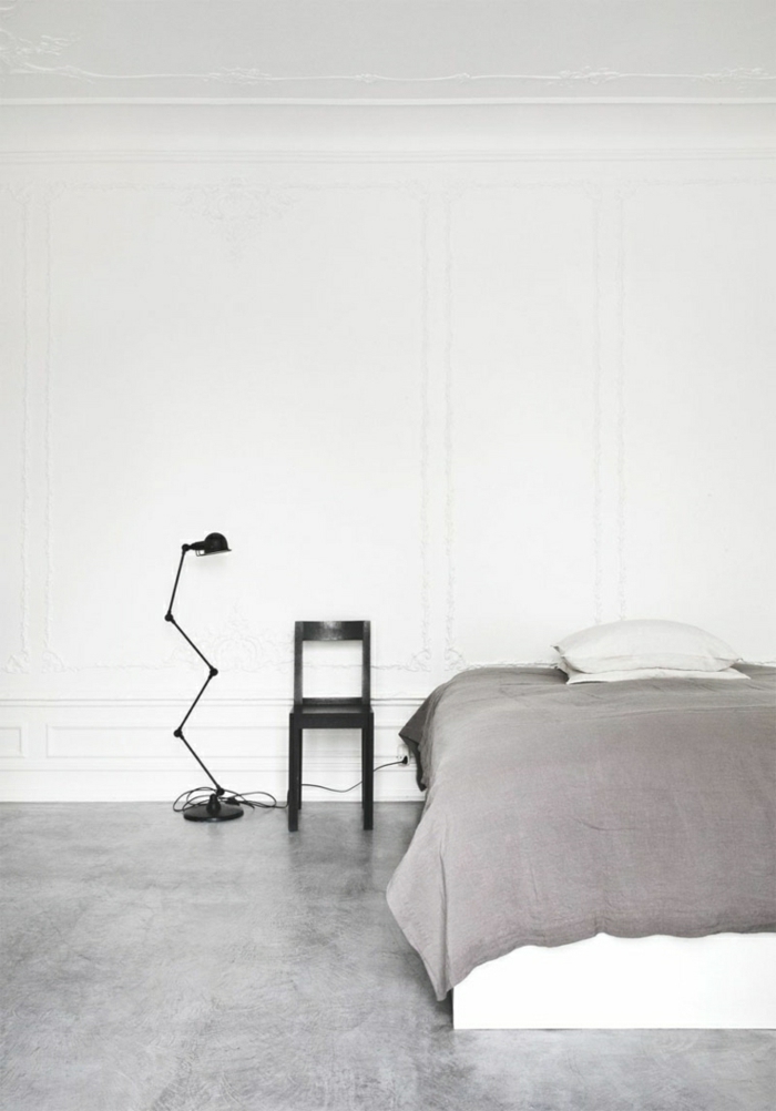 eine weiße Wand, Betonboden, eine graue Decke, ein schwarzer Stuhl, eine schlichte Einrichtung