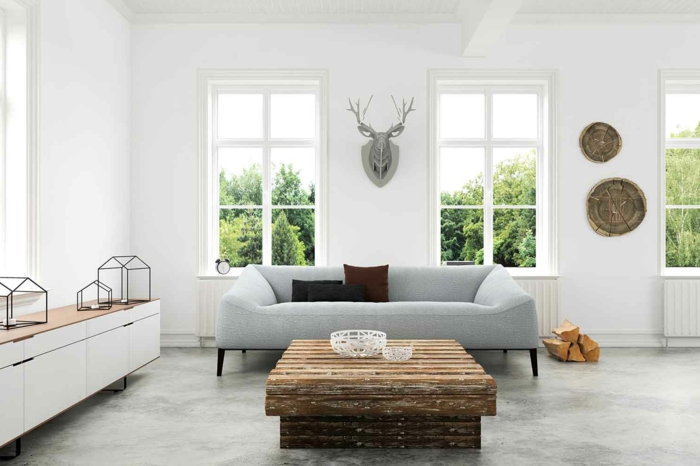 ein schlichtes Wohnzimmer, Hirschkopf an der Wand, ein Couchtisch aus Treibholz, graue Betonbodenfarbe