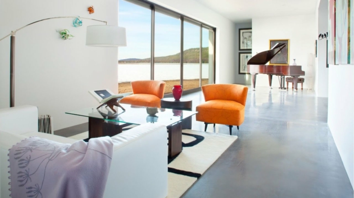 eine kleine Ferienwohnung, zwei orange Stühle, ein weißes Sofa, gläserner Tisch, Betonbodenfarbe