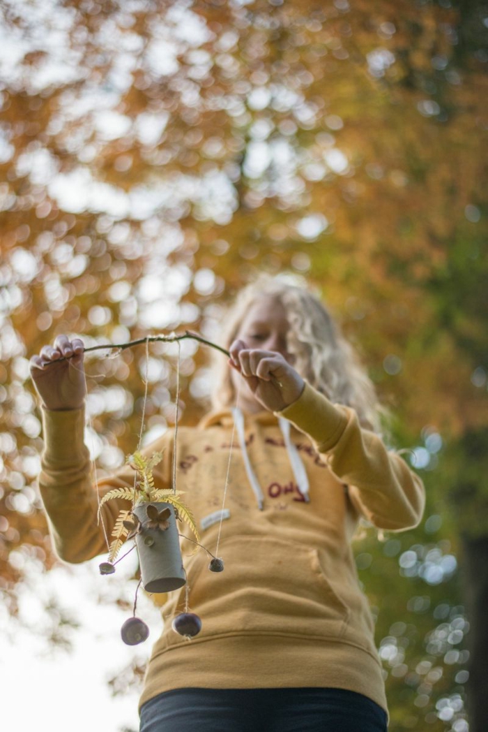 ein Mädchen mit gelber Bluse spielt mit der Drahtpuppe, die zu einem Zweig befestigt ist