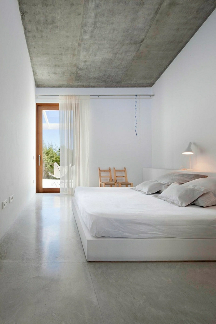 Bodenbelag Betonoptik im Schlafzimmer, ein weißes Bett, zwei kleine Stühle, eine Terrasse