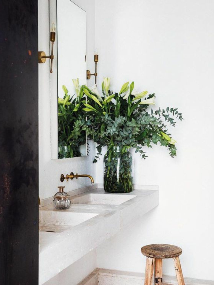 eine Vase mit vielen grünen Zweigen, ein quadrater Spiegel, ein Marmor Waschbecken, ein niedriger Stuhl, Badezimmer Ideen für kleine Bäder