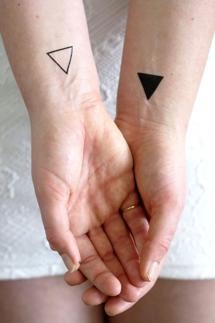 zwei hände mit kleinen handgelenk tattoos mit weißen und schwarzen dreiecken, eine hand mit einem goldenen ring, frauen tattoos handgelenk 