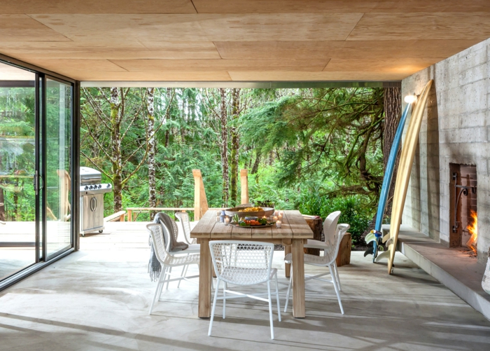 eine schöne Terrasse von Ferienhaus im Wald, ein hölzerner Tisch und ein Kamin, Fußboden Betonoptik