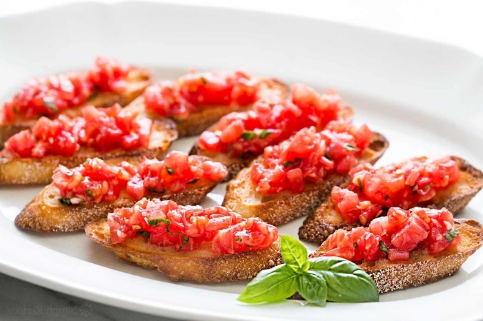 fingerfood ideen, bruschettas mit basilikum und tomaten, großer weißer teller, vorspeise