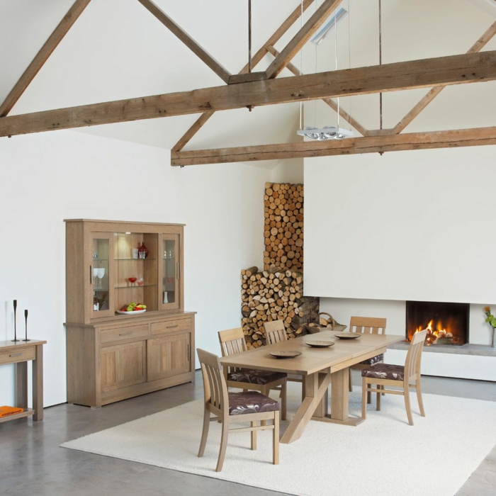 ein Kamin mit Feuer, ein Regal, Tisch und Stühle aus Holz, Balkendach, Betonboden Wohnbereich