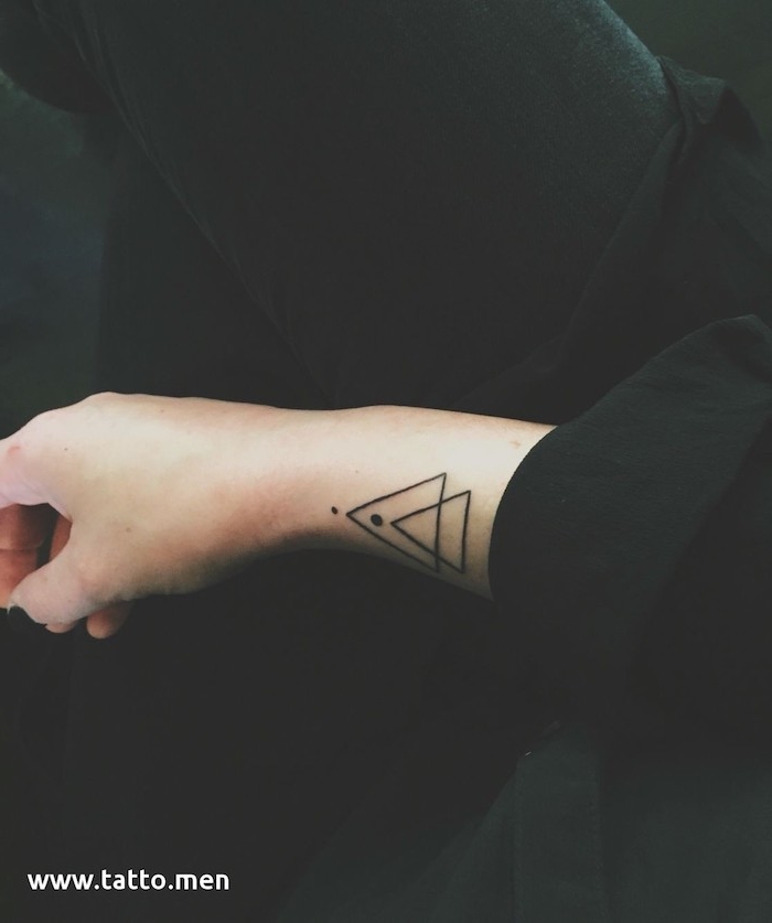 eine hand mit einem schwarzen nagellack und mit einem kleinen schwarzen geometrischen tattoo mit dreiecken und einem schwarzen mond