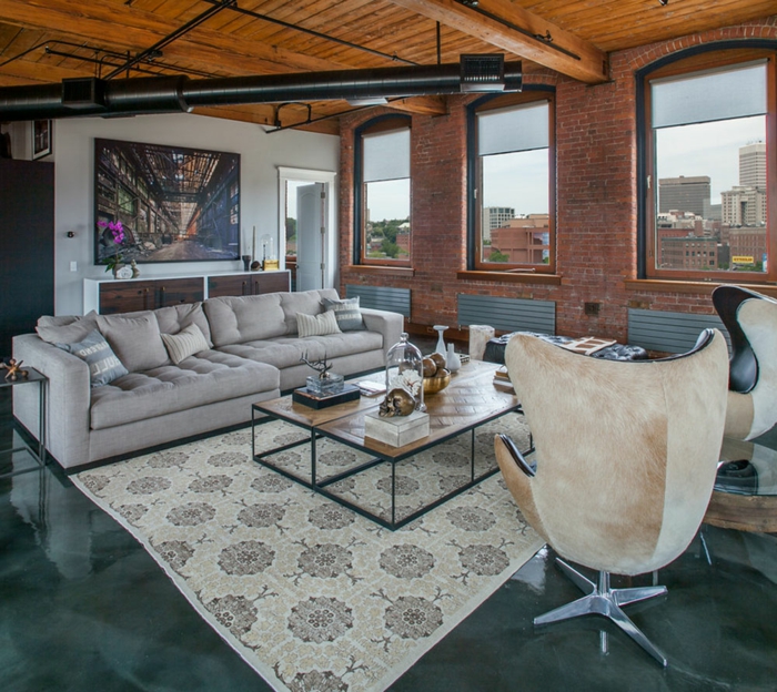 ein graues Sofa, zwei Sessel, ein Teppich mit Blumenmustern, Betonboden Wohnbereich