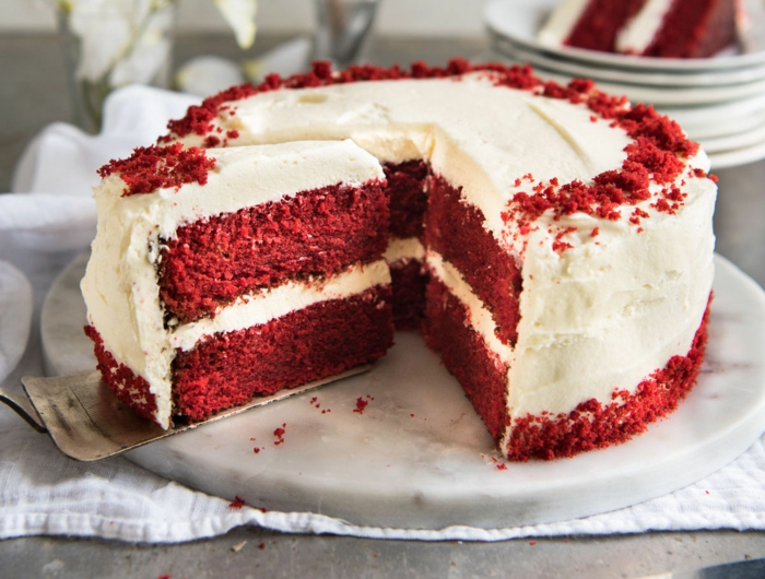 weiße Creme, rote Böden, rote Dekoration darauf, Kuchen backen, weiße Platte