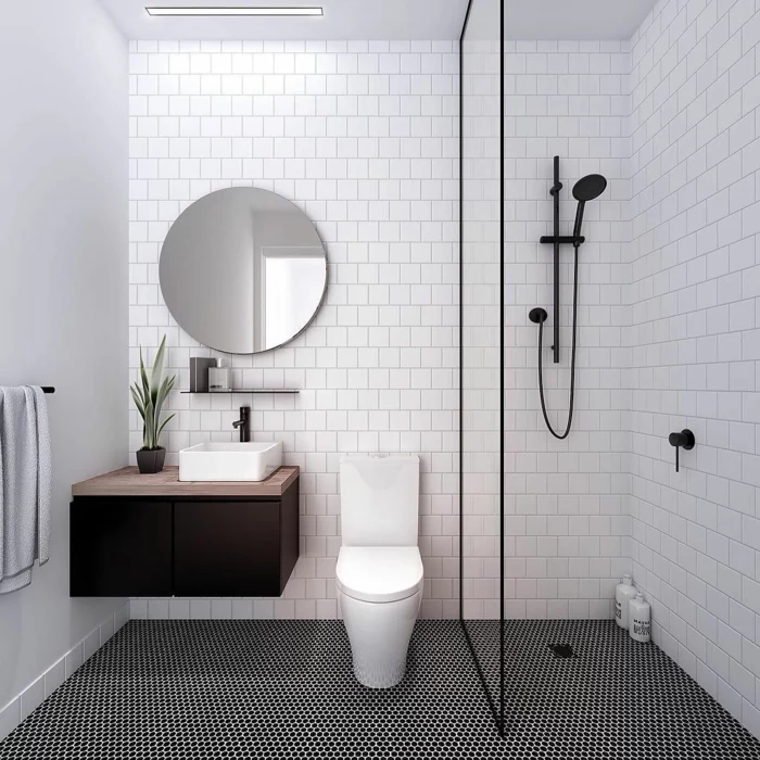 ein bildschönes Badezimmer mit rundem Spiegel, schwarze Mosaikfliesen am Boden, günstige Badmöbel für kleine Bäder