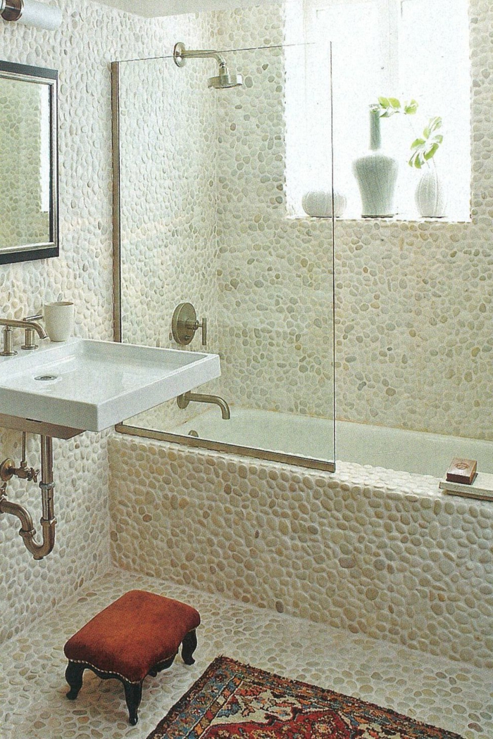 ein Badezimmer mit Narsteinoptik Mosaikfliesen, ein kleiner Waschbecken, ein Spiegel mit schwarzen Rahmen