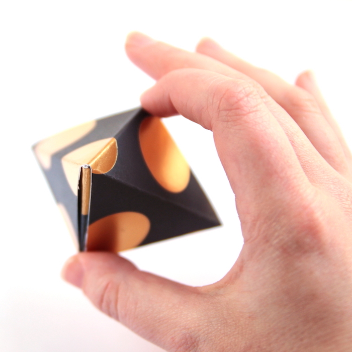 selbstgemachte origami schachtel aus schwarzem papier mit goldenen punkten, pyramide