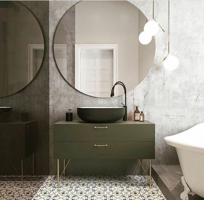 großer runder Spiegel, ein schwarzes Waschbecken und graue Unterschänke, Bodenfliesen mit Mustern, graue Wand