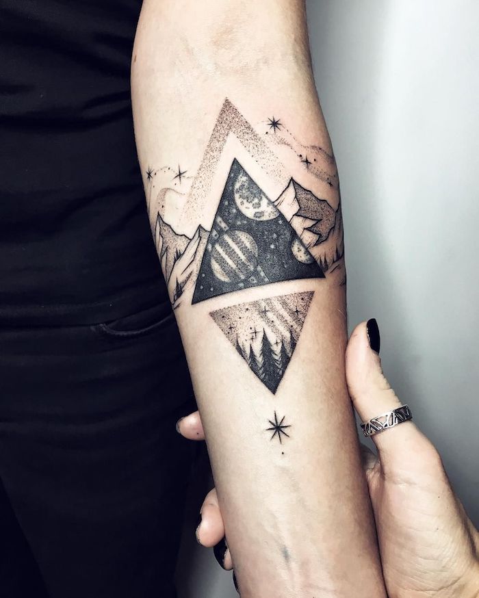 eine hand mit einem ring und einem schwarzen nagellack, hand mit einem schwarzen tattoo mit dreiecken und einem himmel mit schwarzen sternen und bergen und einem schwarzen himmel mit planeten und sternen 