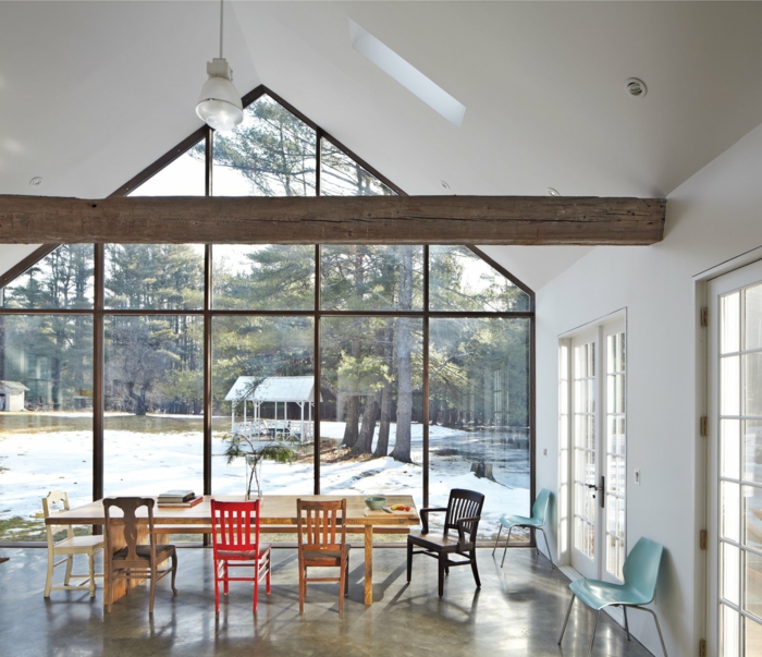 ein langer Tisch, bunte Stühle, eine Glaswand, eine Balke, Ferienhaus, Betonboden Wohnbereich