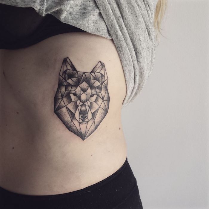 kleines schwarzes tattoo mit einem wolf mit schwarzen augen und einer schwarzen nase und mit vielen schwarzen geometrischen formen, eine frau mit einem wolf tattoo