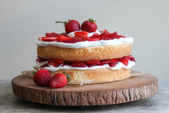 ein Kuchen mit weißer Creme und Erdbeeren als Dekoration, auf Holzplatte
