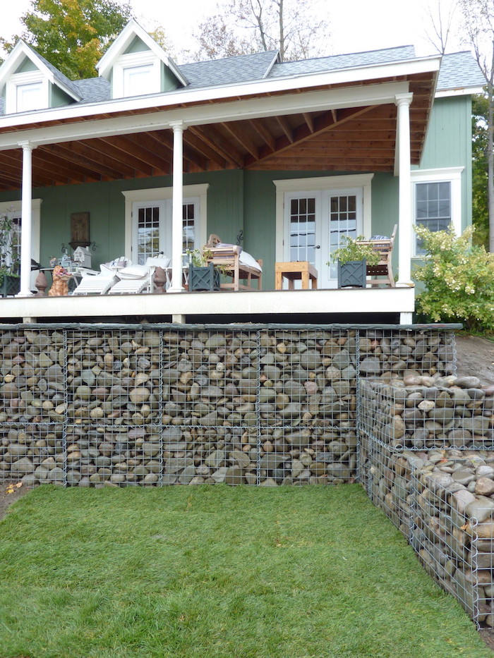 sichtschutz terrasse selber bauen, ein haus mit garten mit gabionen sichtschutz aus grauen kleinen steinen und mit einem grünen rasen