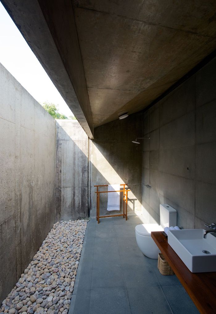 ein haus mit terrasse mit grauen wänden und einer outdoor dusche, weißen waschbecken und einem boden aus vielen kleinen steinen