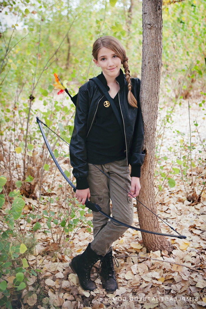 eine junge Katniss Everdeen mit Boden und Pfeile, im Wald, Mädchen mit Zopf und Brösche
