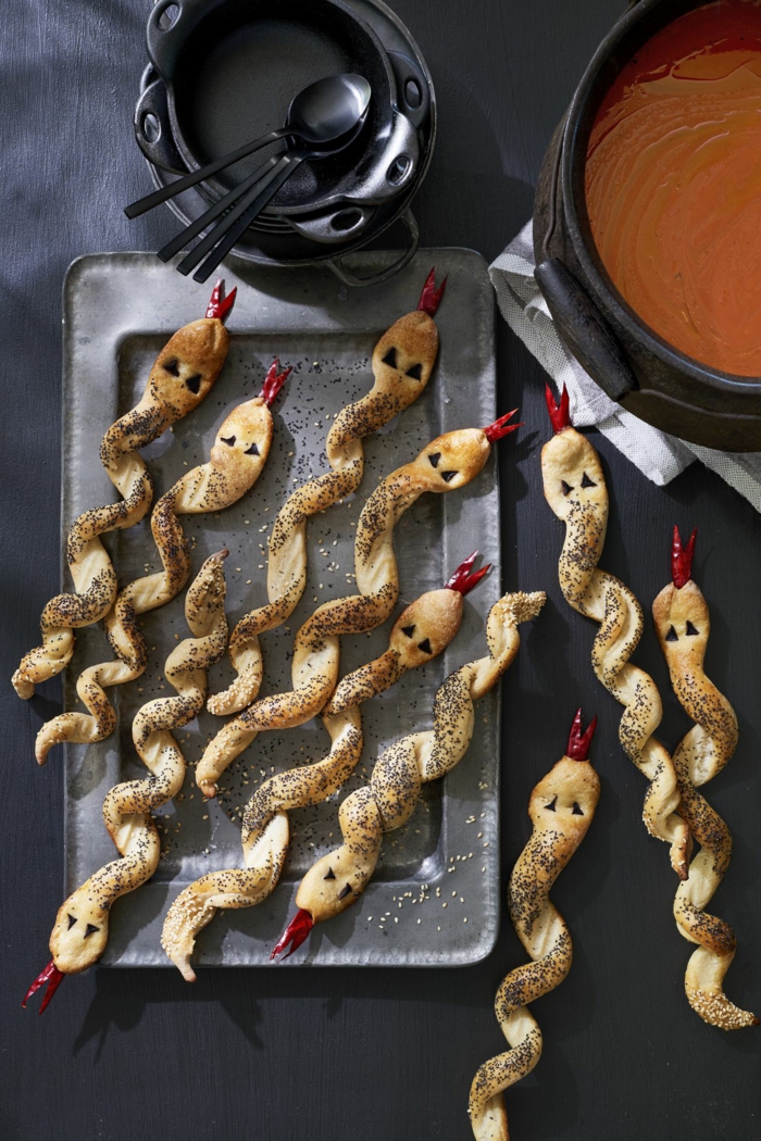 Schlangen aus Teig mit kleinen herausgesteckten Zungen aus Paprika, mit Quinoa bestreut, Halloween Menü