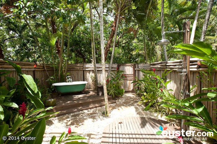 garten mit einem zaun aus vielen braunen bambus stäben, eine kleine grüne badewanne und ein sichtschutz zaun aus holz und sichtschutz pflanzen 