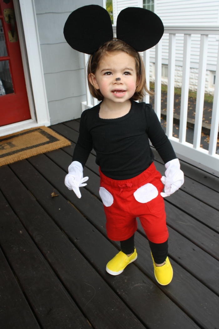 ein kleines Mädchen als Mickey Maus maskiert, rote Hosen, große schwarze Ohren und gelbe Schuhen