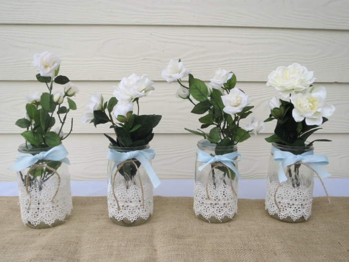 vier Vasen mit weißen Rosen, blaue Schleifen und Spitze darum, alles für die Hochzeit