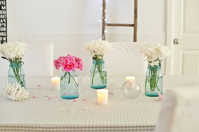 vier Vasen in blauer Farbe, drei voller weiße Blumen und eine voller rosa Blumen, Kerzen dazwischen, Deko für Hochzeit
