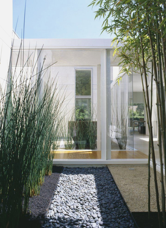 blauer himmel und ein haus mit weißen wänden und kleiner steingarten mit grauen kleinen steinen und mit grünen pflanzen und langen bambus stäben