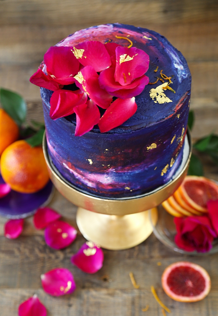 kuchen verzieren, geburstagstorte dekoriert mit creme in lila, blau und rot und rosenblätter, torte mit roter orange 