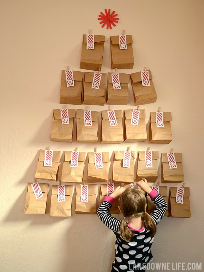 ein Mädchen hängt Tüte von dem Adventskalender, braune Tüten mit gestreiften Anhänger, DIY Adventskalender