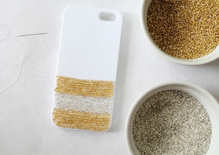 DIY Anleitung für Handyhülle erstellen, aufgeklebte Glasperlen in Gold und Weiß, kleine Nadel und weißer Faden