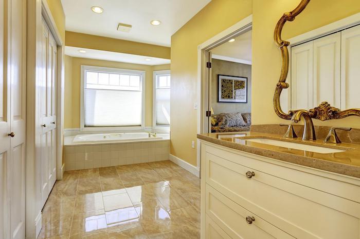 großes badezimmer mit gelben wänden und einem spiegel und fenstern. weiße freistehende badewanne
