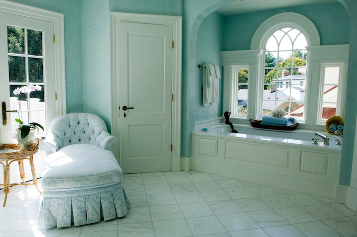 ein tisch mit vasen mit weißen blumen, ein badezimmer mit grünen wänden und fenstern und einer weißen badewanne und weißer tür 