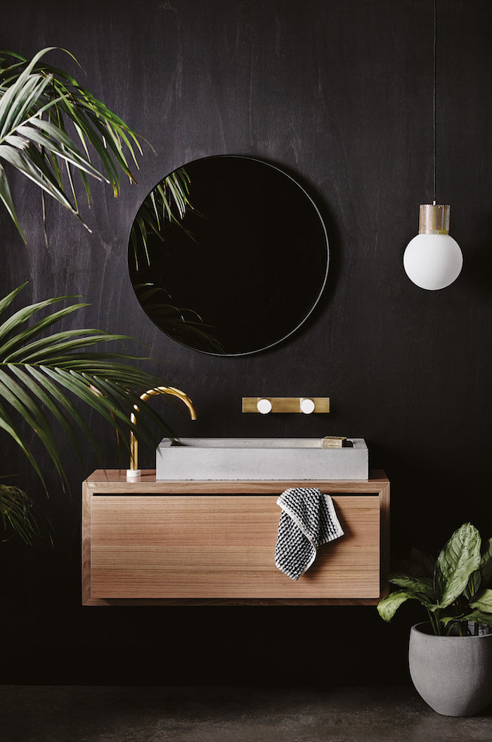 schwarze wand im badezimmer mit einem schwarzen spiegel und einer weißen vase mit grünen pflanzen, ein braunes waschbecken aus holz, weiße badezimmer lampe