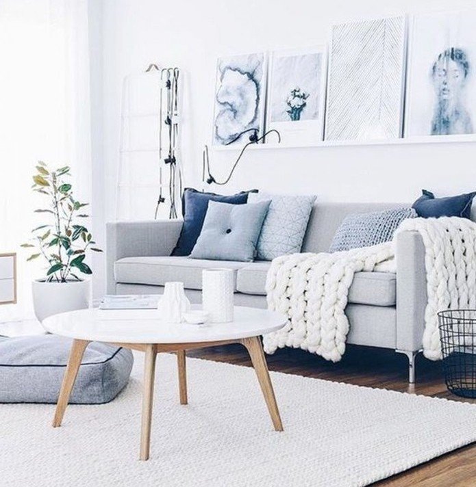 ein graues Sofa, ein weißer runder Tisch, graue Kissen, eine weiße Leistne mit modernen Bildern