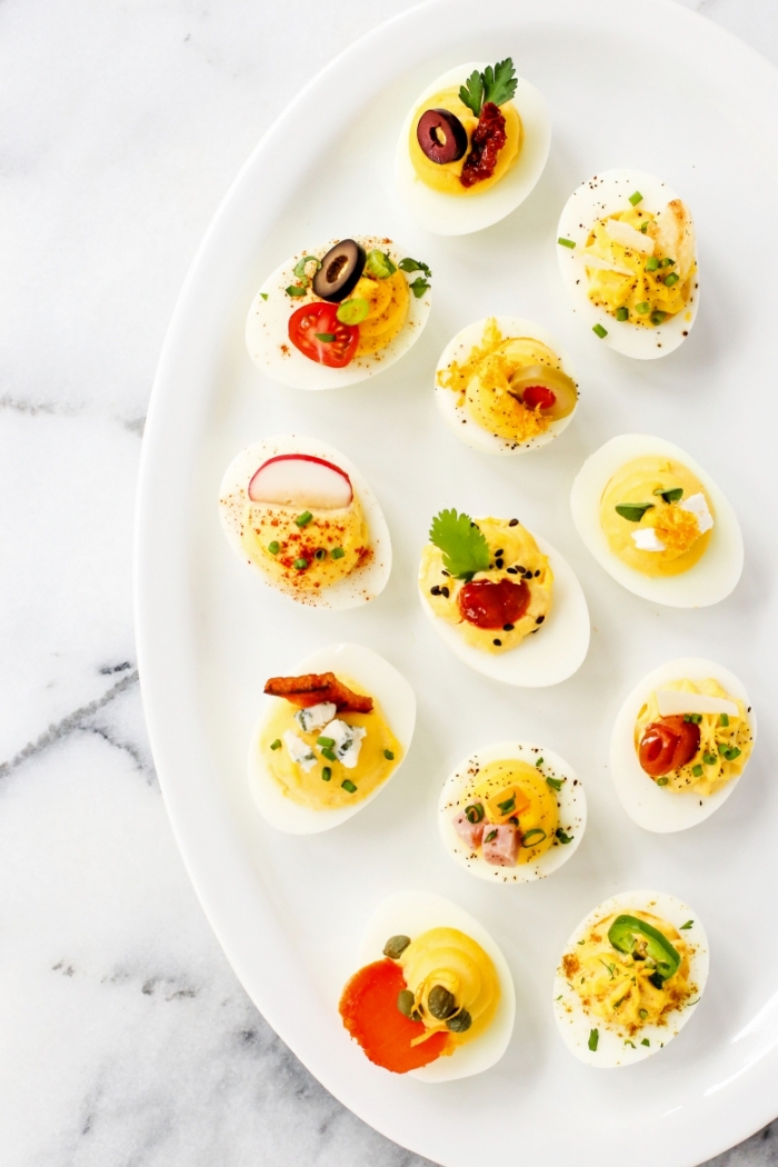 essen für gäste, weißer ovaler teller, einfache vorspeise, eier mit verschiedenen gewürzen, oliven