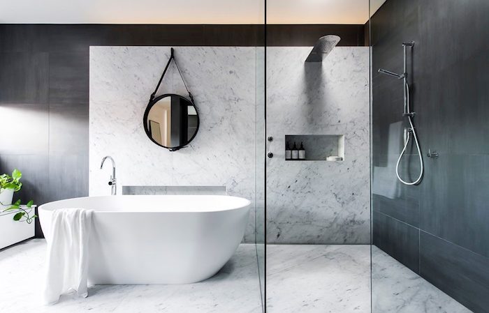 ein spiegel und kleine weiße freistehende badewanne im badezimmer mit weißen und schwarzen wänden und badezimmer fliesen