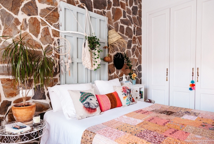 macrame dekoration in dem schlafzimmer, buntes ethno design, orientalisch dekorieren, steinwand, ein blumentopf mit pflanze am bett