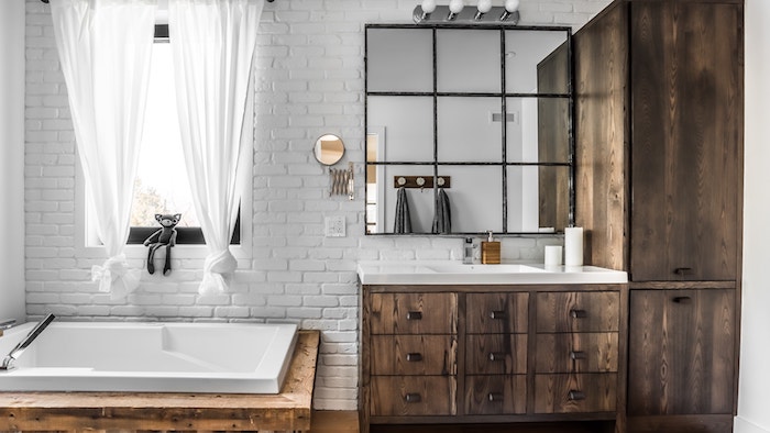 badezimmer mit fenster und einer weißen wand aus weißen steinen und weißen vorhängern, ein spiegel und badezimmer spiegelschrank 