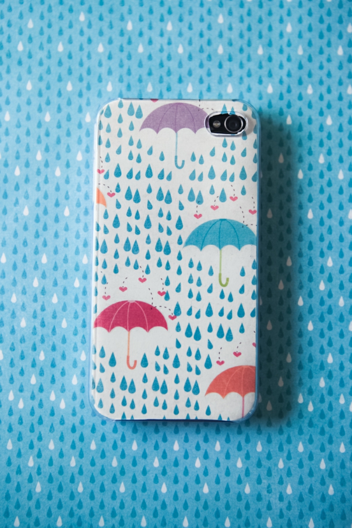 ein Handy mit kleinen Regentropfen, die sich in Herzen verwandeln, bunte Regenschirme, personalisierte Handyhülle