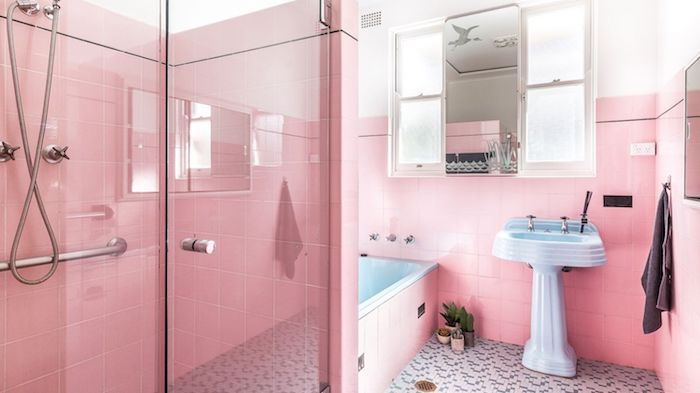 pinkes badezimmer mit pinken wänden mit vielen kleinen pinken badezimmer fliesen, ein blaues waschbecken und ein spiegel und eine dusche aus metall