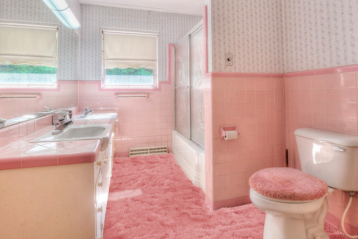 pinkes badezimmer mit einem pinken teppich und wänden mit pinken und weißen fliesen und ein pinkes waschbecken