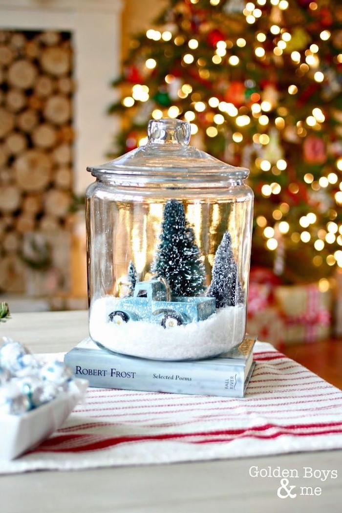 Große Schneekugel auf Buch, blaues Spielzeugauto und Weihnachtsbäume darin, mit künstlichem Schnee 