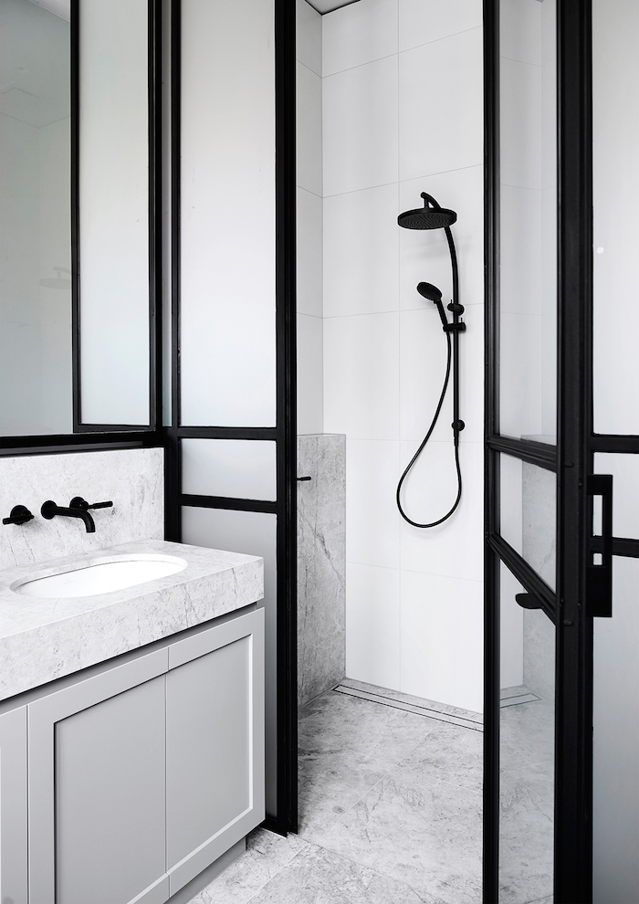 ein badezimmer mit weißen und schwarzen wänden und ein weißes waschbecken und eine schwarze dusche aus metall